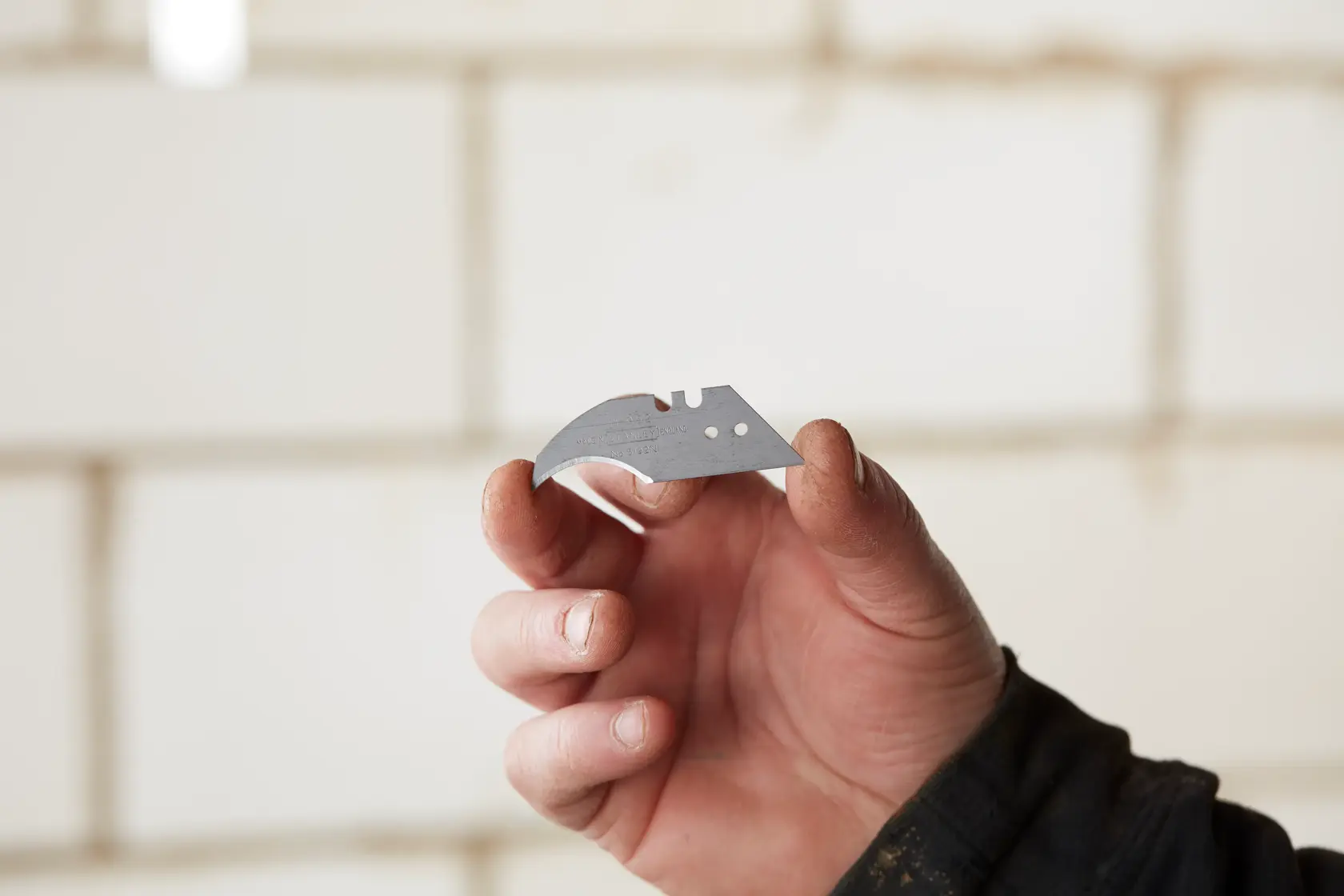 Photo of STANLEY 0-11-952 utility knife blade held in hand, showing sharp edge and mounting holes.