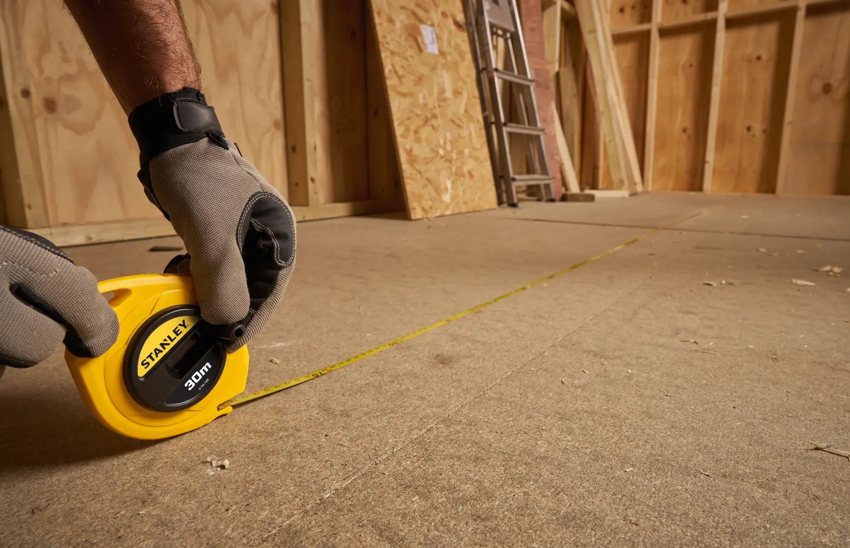 STANLEY 0-34-108 measuring tape, yellow, used on construction floor, person wearing gloves.