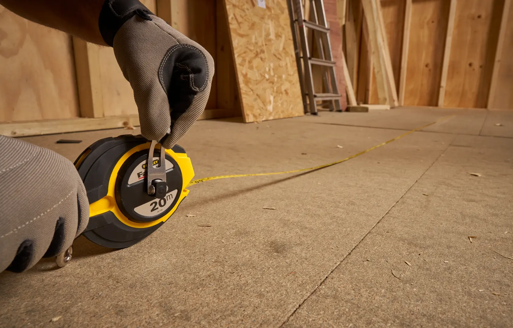 Photo of STANLEY 0-34-133 measuring tape reel in use on a construction floor, yellow tape extended.