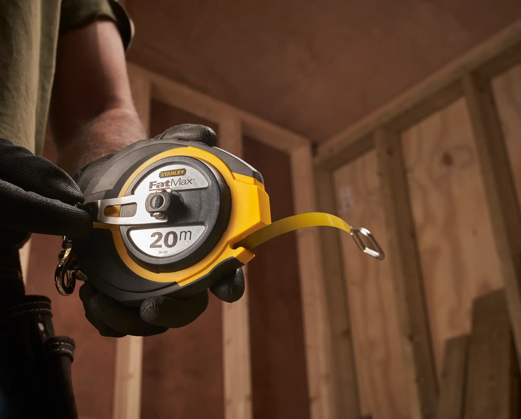 Photo of STANLEY 0-34-133 FatMax 20m tape measure held by gloved hand in construction setting.