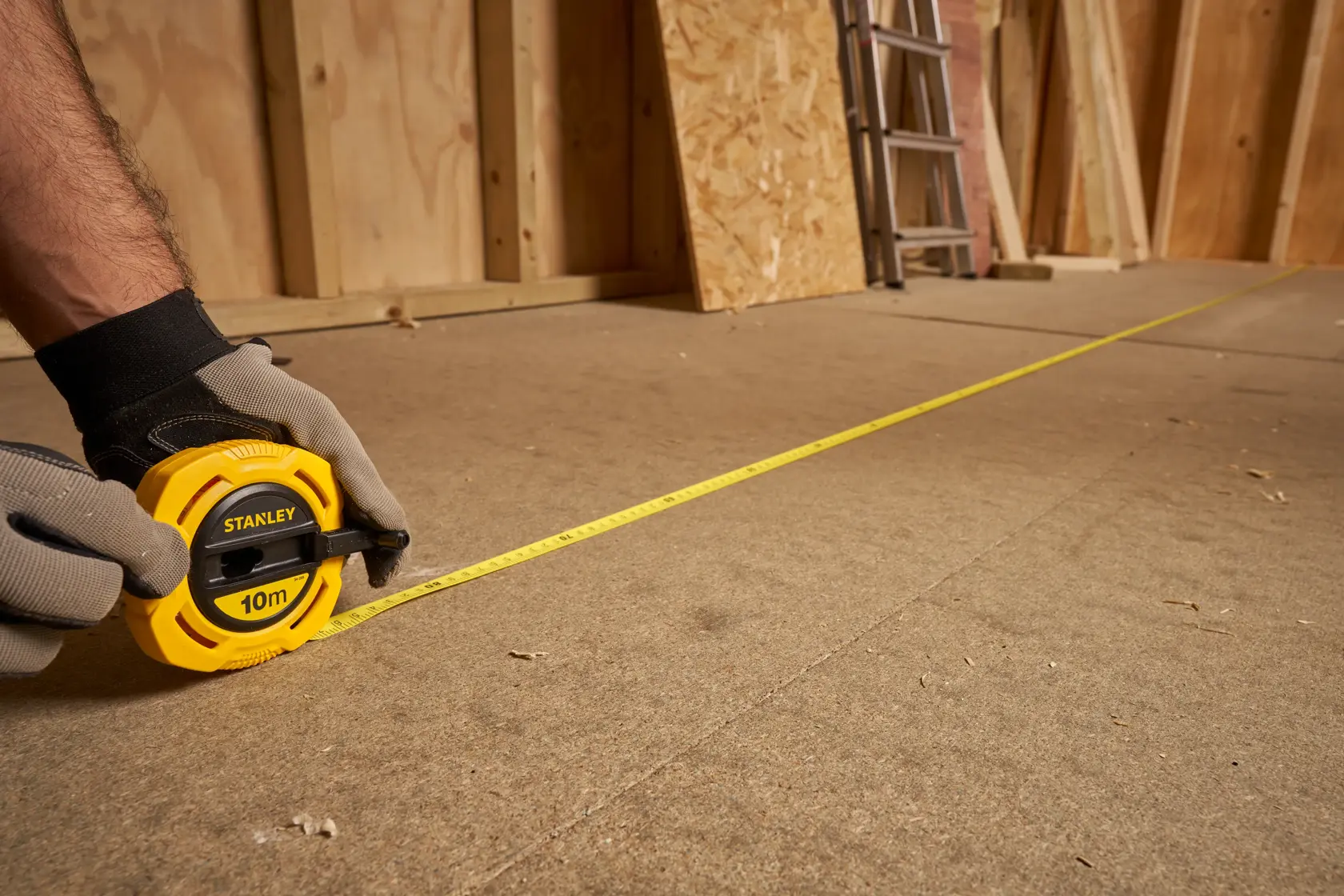 Photo of STANLEY 0-34-295 yellow tape measure extended across a construction floor, held by gloved hands.