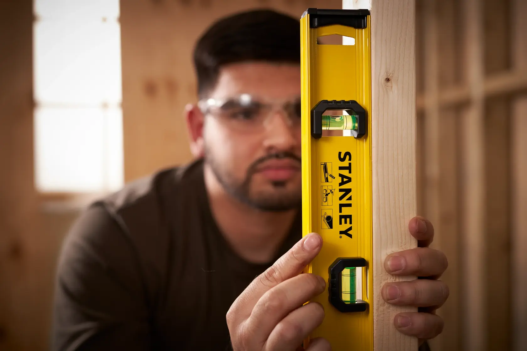 Photo of STANLEY 0-42-072 level tool in use, yellow body, visible vials, held against wooden beam.