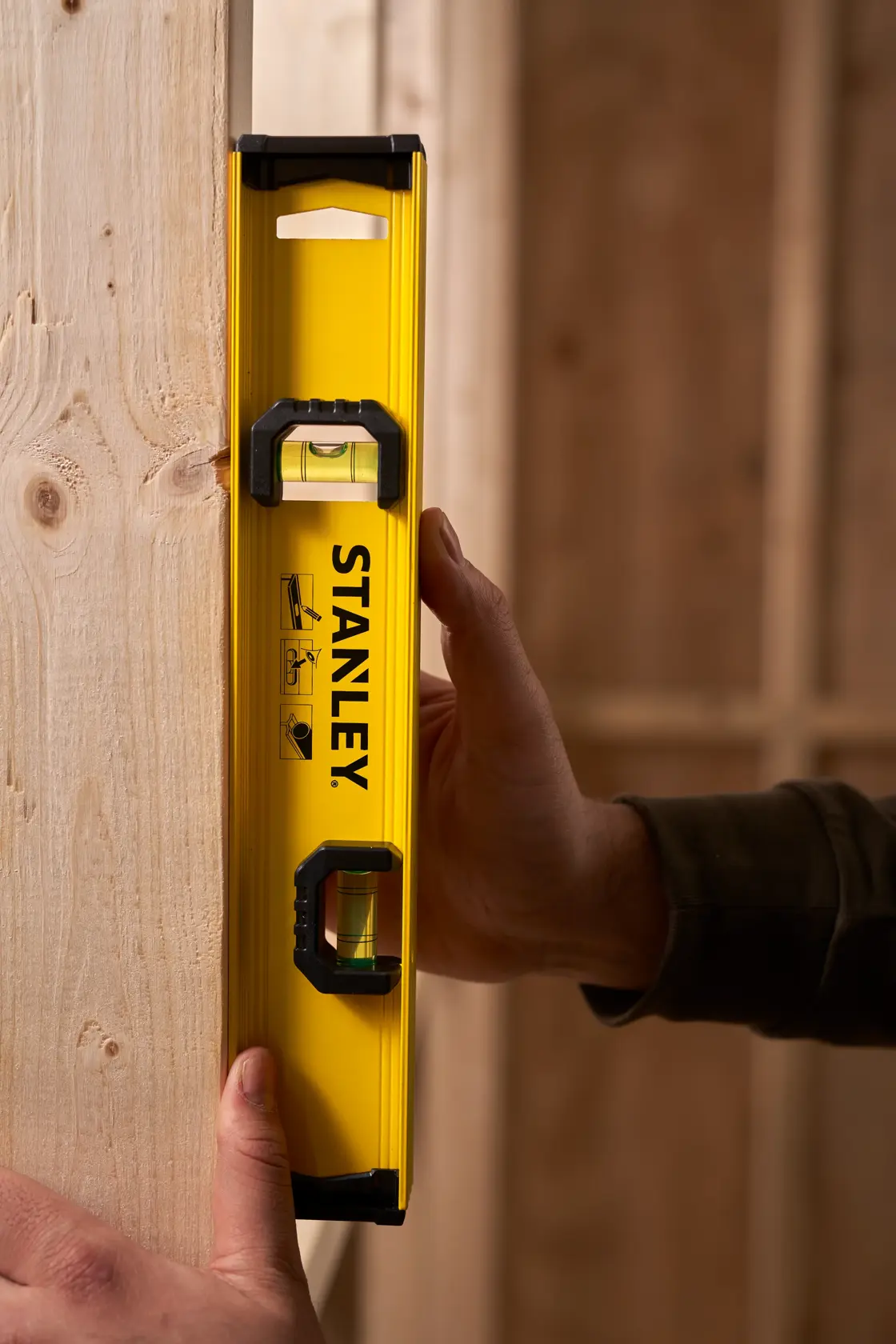 STANLEY 0-42-072 yellow spirit level held vertically against wooden beam, product photography.