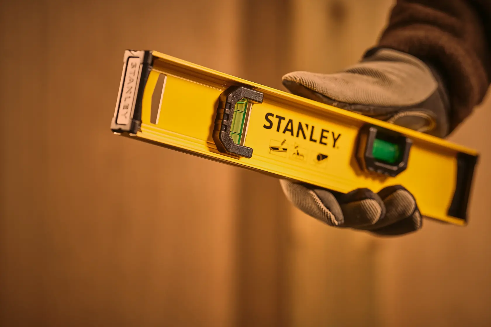Stanley 0-42-072 spirit level photography, yellow body, held by gloved hand, close-up view.