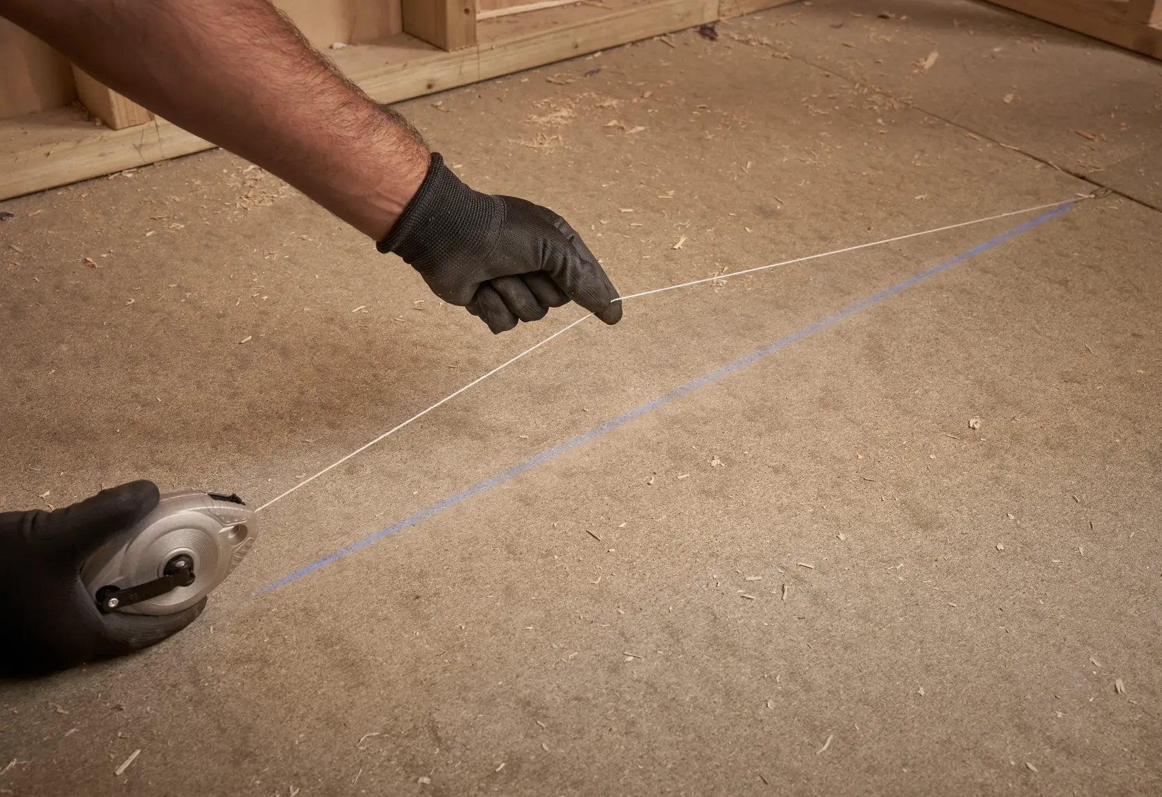 STANLEY 0-47-100 chalk line reel in use, hands with gloves marking a straight blue line on a plywood floor.