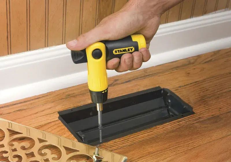 STANLEY 0-63-022 ratcheting screwdriver in use adjusting floor vent cover on hardwood floor.