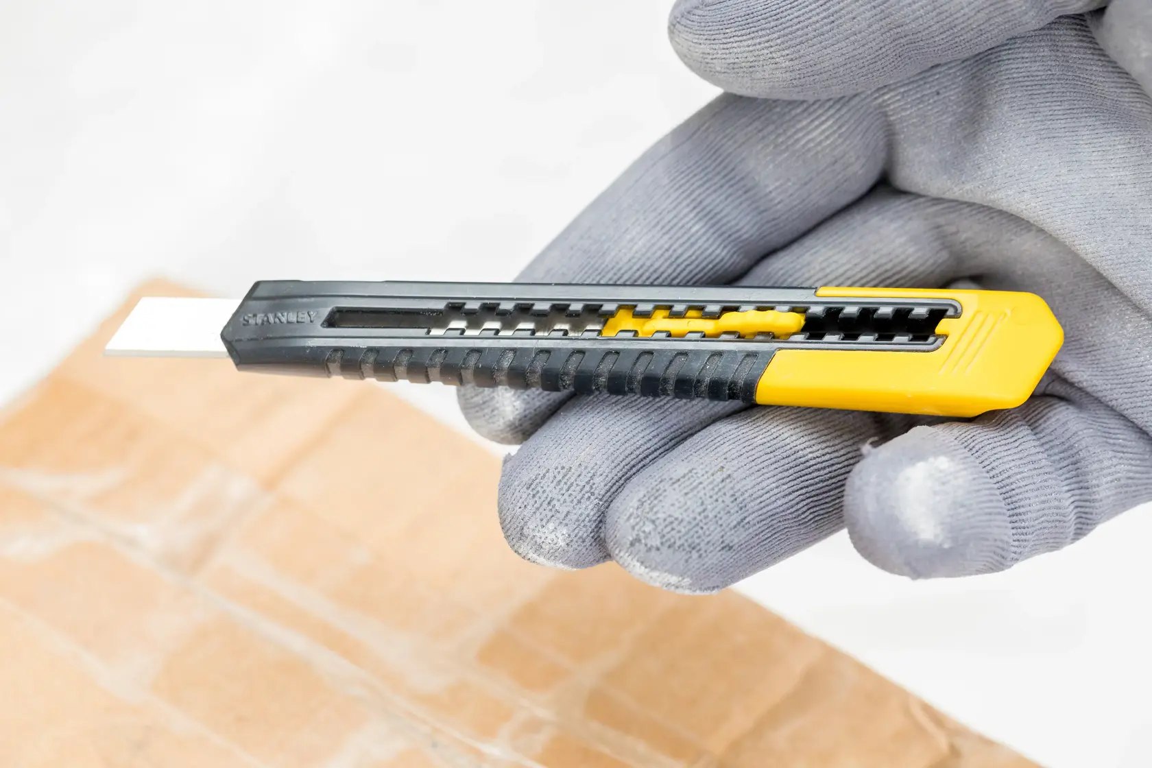 STANLEY 1-10-150 utility knife with yellow and black handle held in gloved hand, cutting cardboard.
