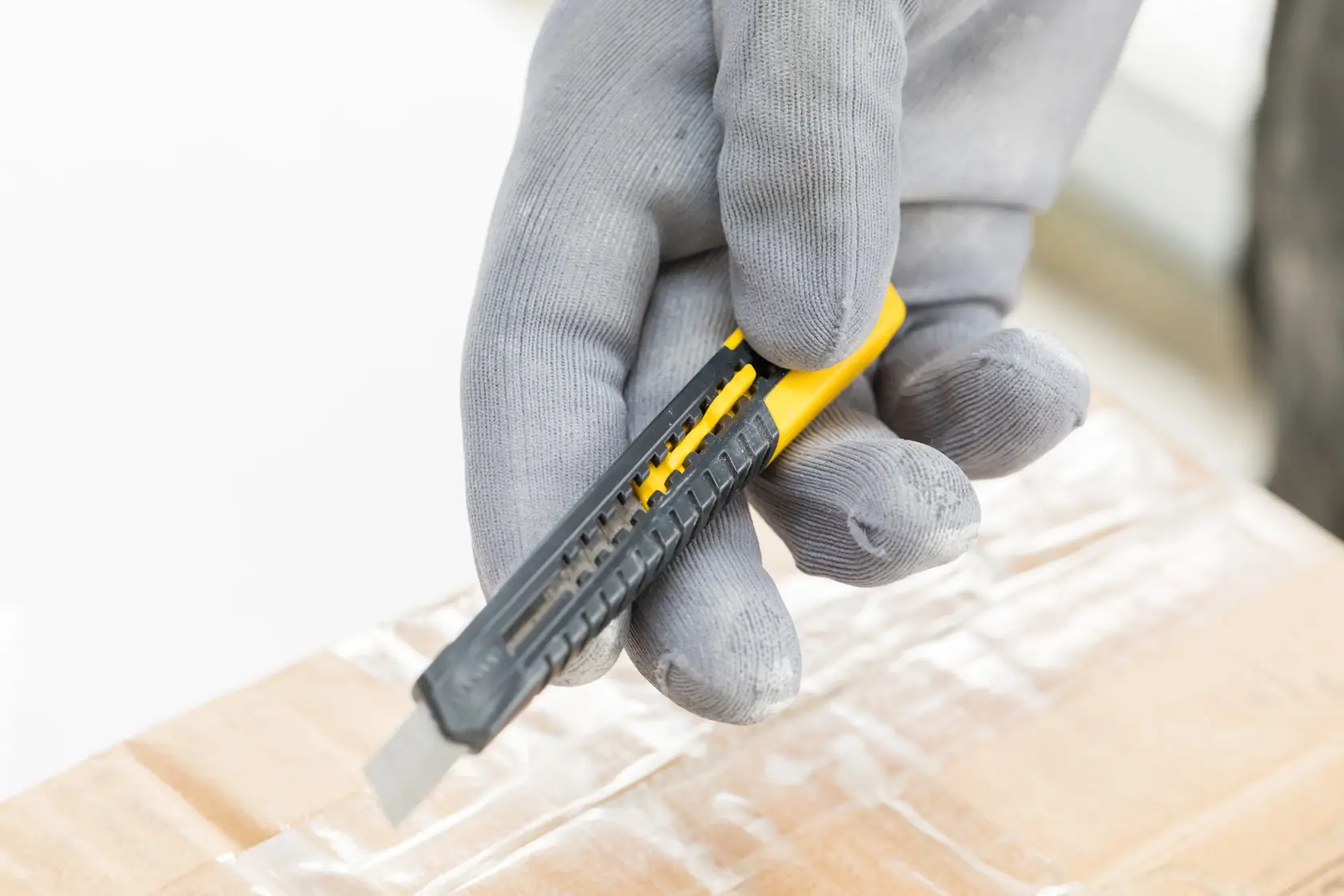 Photo of STANLEY 1-10-150 utility knife in a gloved hand cutting cardboard, close-up angle.