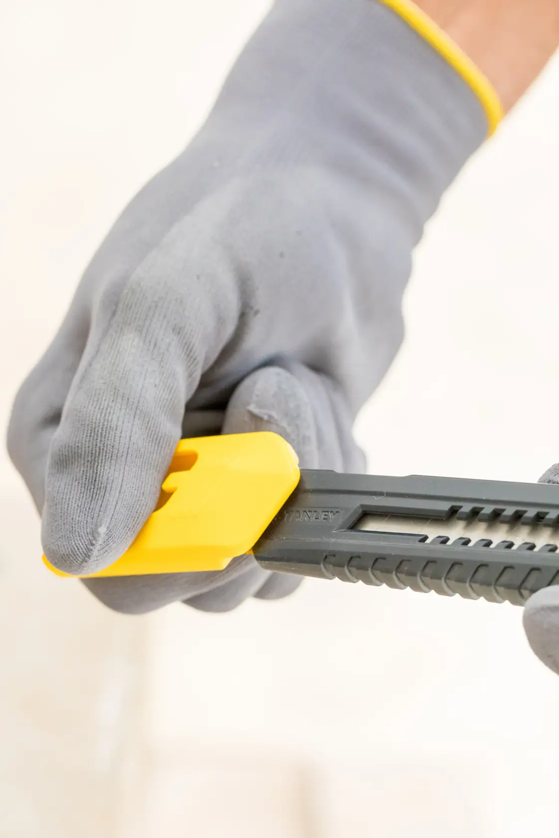 Photo of a gloved hand adjusting the yellow blade lock on a STANLEY 1-10-151 utility knife.