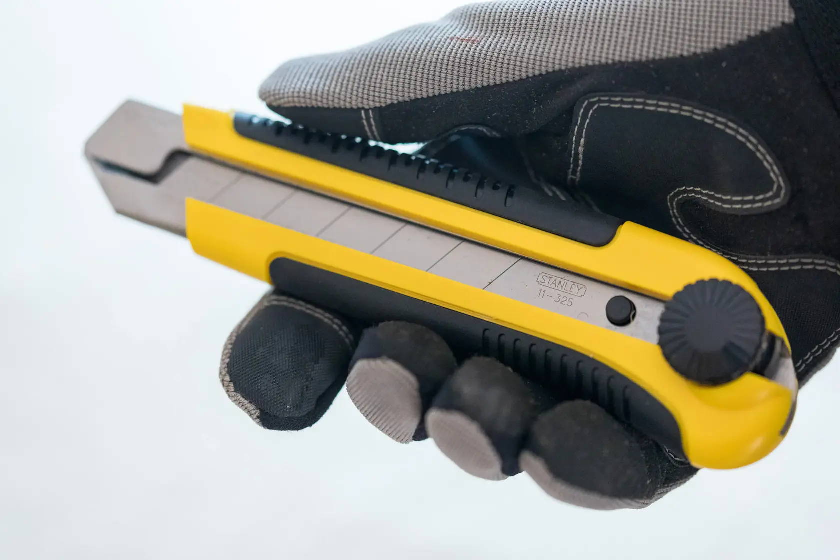 STANLEY 1-10-425 utility knife in yellow and black, side angle, held by a gloved hand.