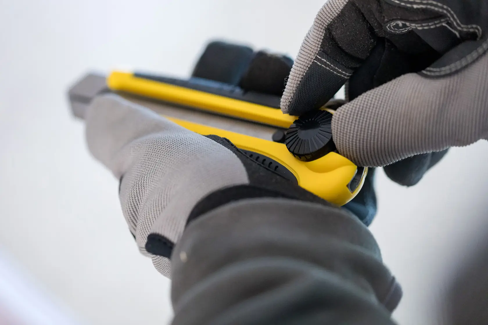 STANLEY 1-10-425 utility knife in use, close-up of gloved hands adjusting yellow knife.