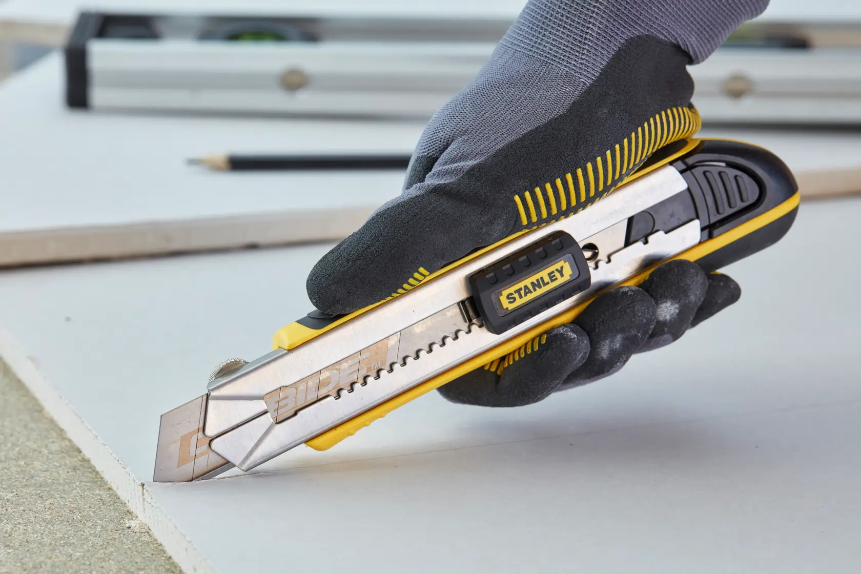 Stanley 1-10-481 utility knife in use, yellow and silver, held by gloved hand cutting drywall.
