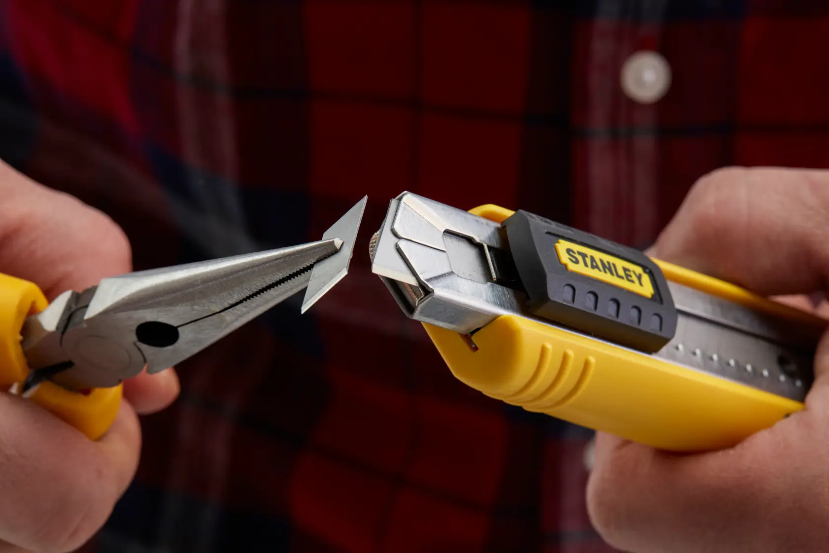 STANLEY 1-10-481 utility knife with yellow handle, blade being changed with pliers, close-up view.