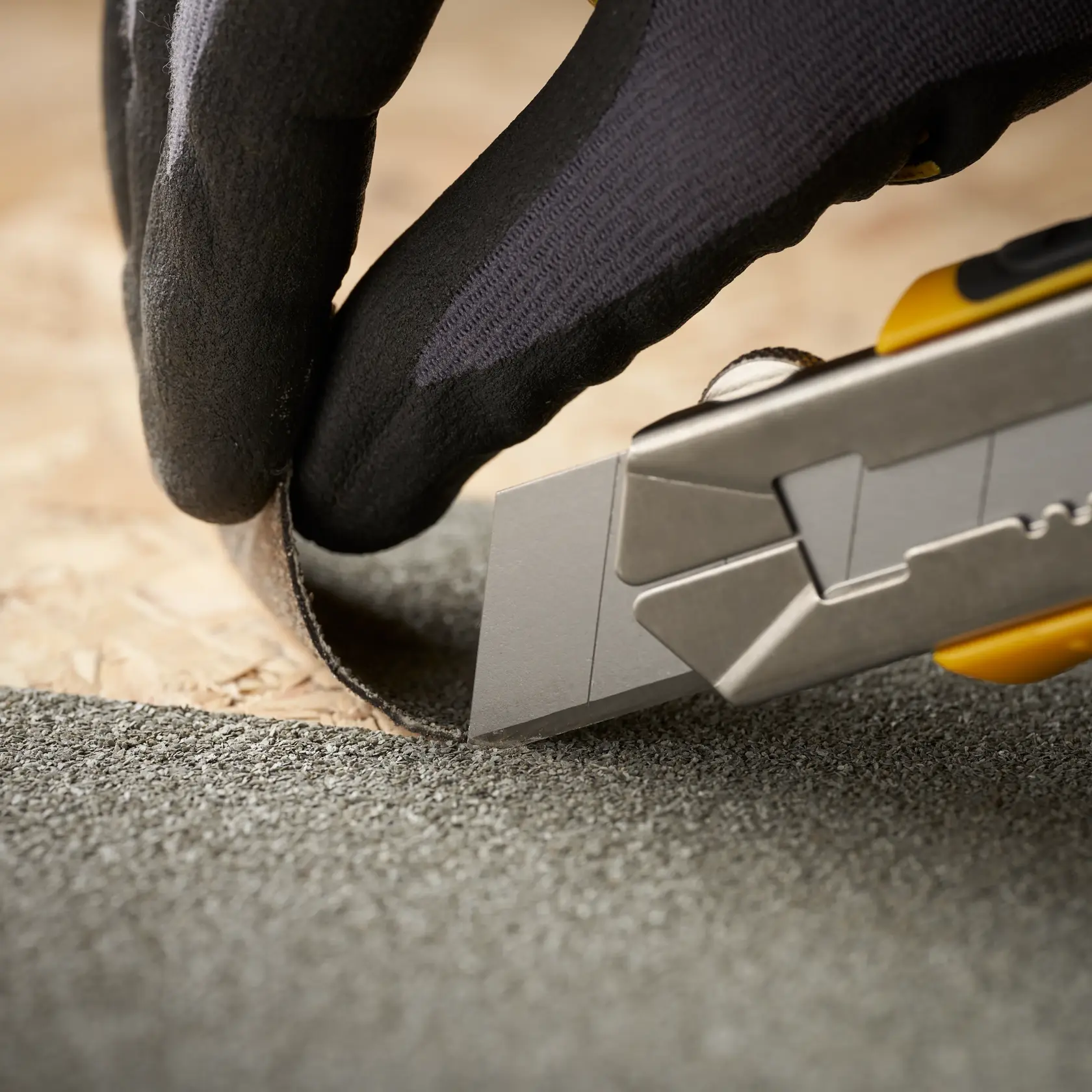 STANLEY 1-11-325 utility knife cutting roofing material, close-up side view, gloved hand holding material.