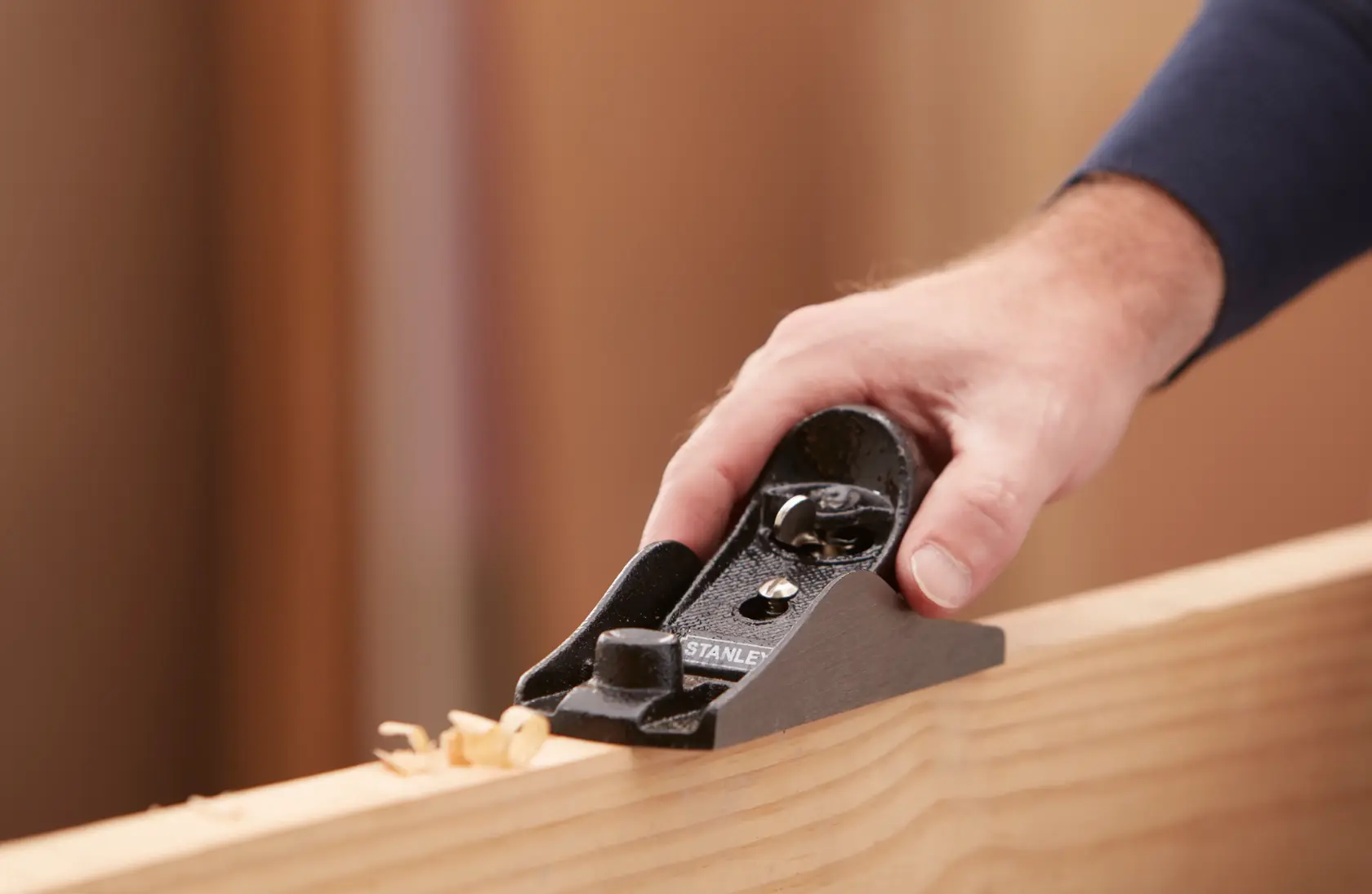 STANLEY 1-12-220 block plane being used to smooth wooden edge, close-up with hand on tool.