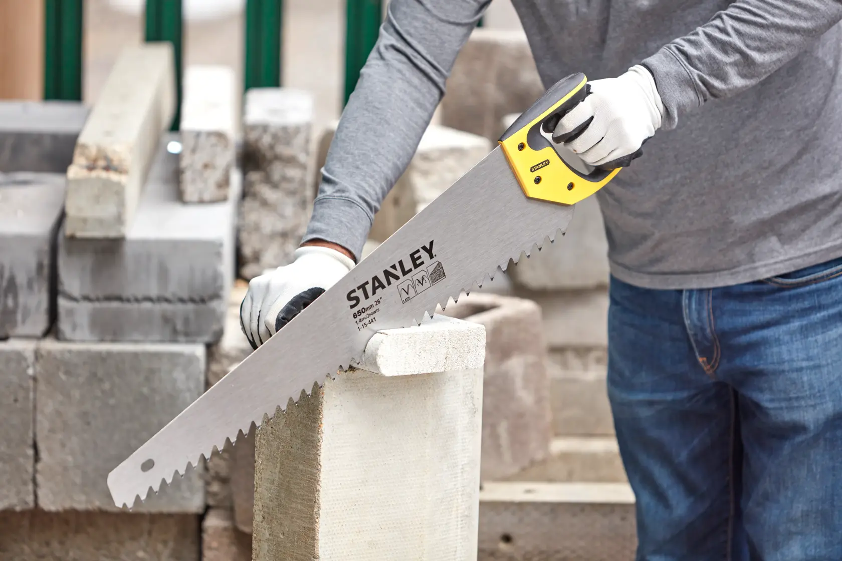 Photo of STANLEY 1-15-441 hand saw cutting a concrete block, yellow handle, construction context.