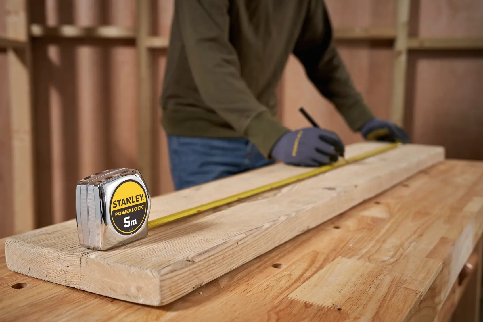 STANLEY 1-33-195 tape measure on wooden beam, worker marking measurements in workshop.