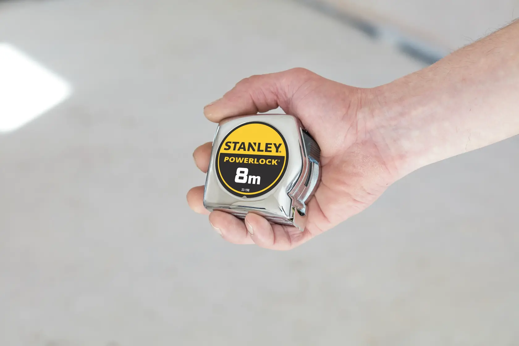 Photo of STANLEY 1-33-198 PowerLock 8m tape measure held in hand, silver and yellow, product category photography.