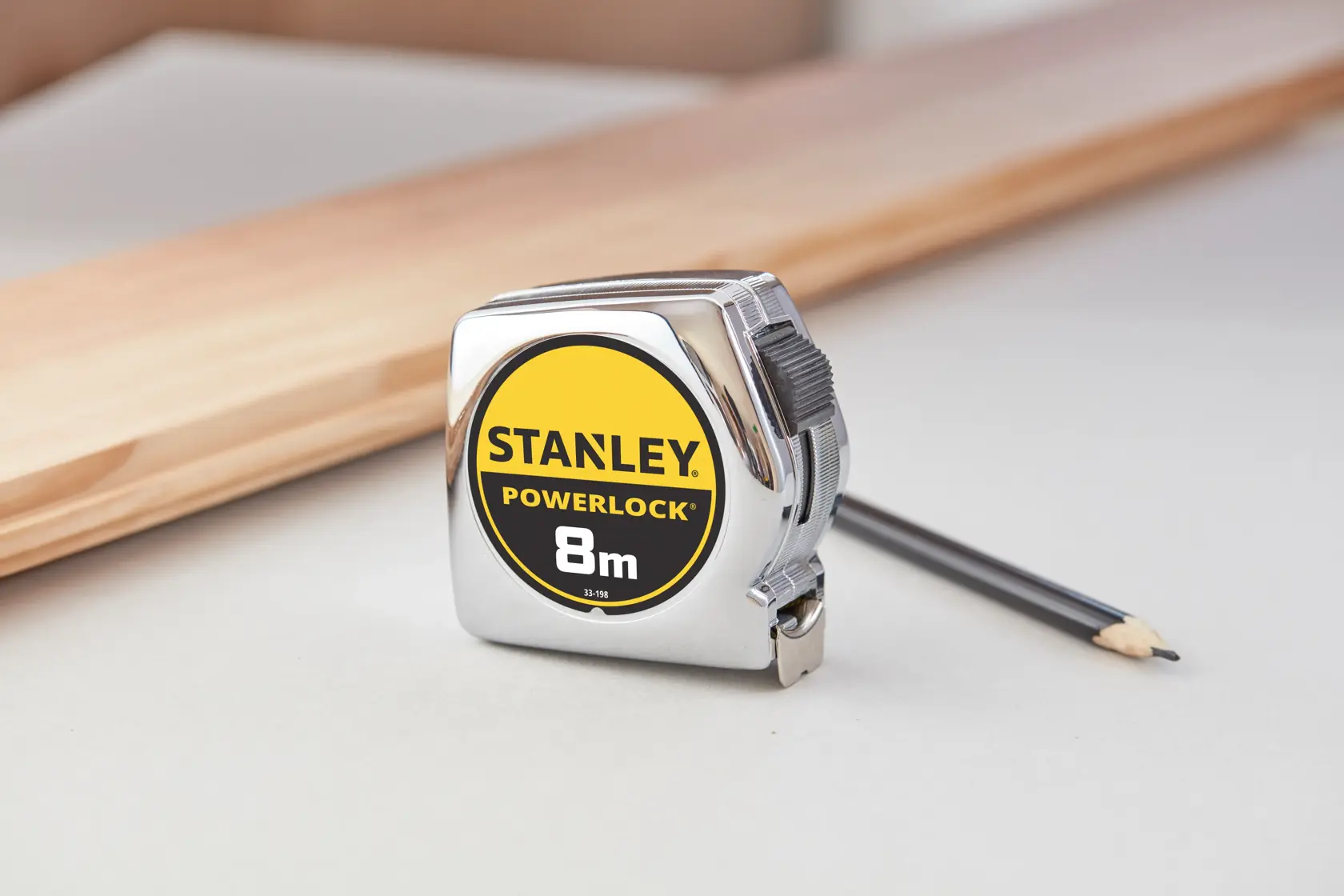 STANLEY 1-33-198 PowerLock 8m tape measure with chrome case, shown on table beside pencil and wood.
