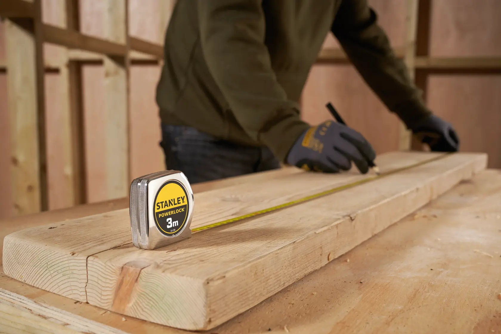 STANLEY 1-33-238 tape measure on wooden plank, person marking wood with pencil, construction context.