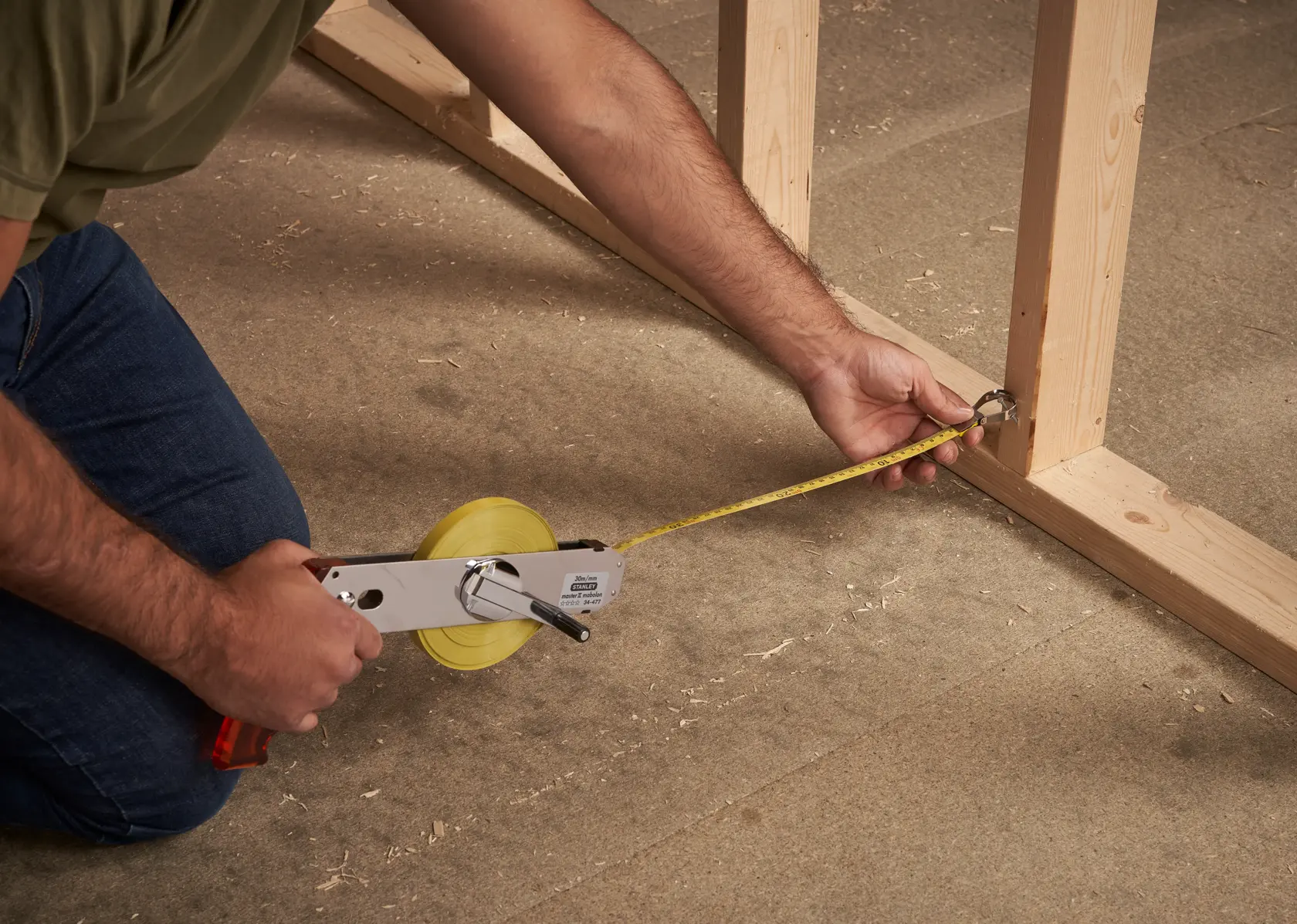 STANLEY 1-34-477 measuring tape reel in use on construction framing, angled side view.