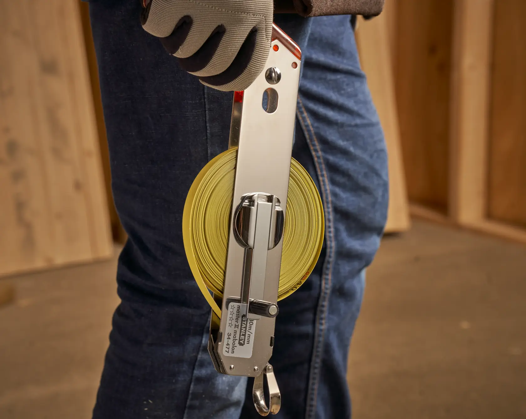 STANLEY 1-34-477 open reel tape measure with yellow blade, held by a gloved hand at a construction site.