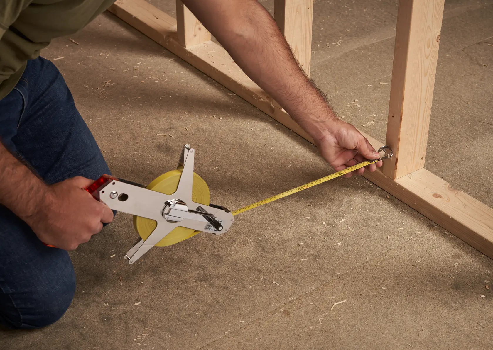 STANLEY 1-34-478 long measuring tape in use on a construction site, measuring wooden frame on the floor.