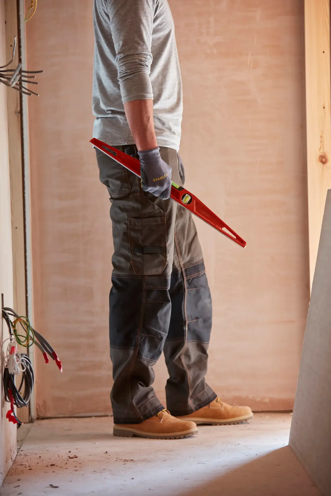 Photo of a person wearing work gloves holding a STANLEY 1-42-314 level tool at a construction site.