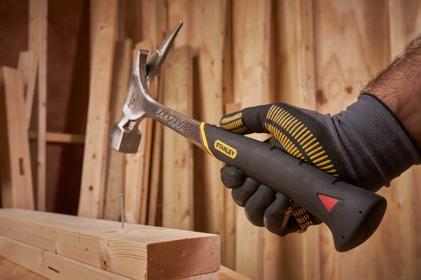STANLEY 1-51-937 claw hammer in gloved hand, driving nail into wood, workshop background.