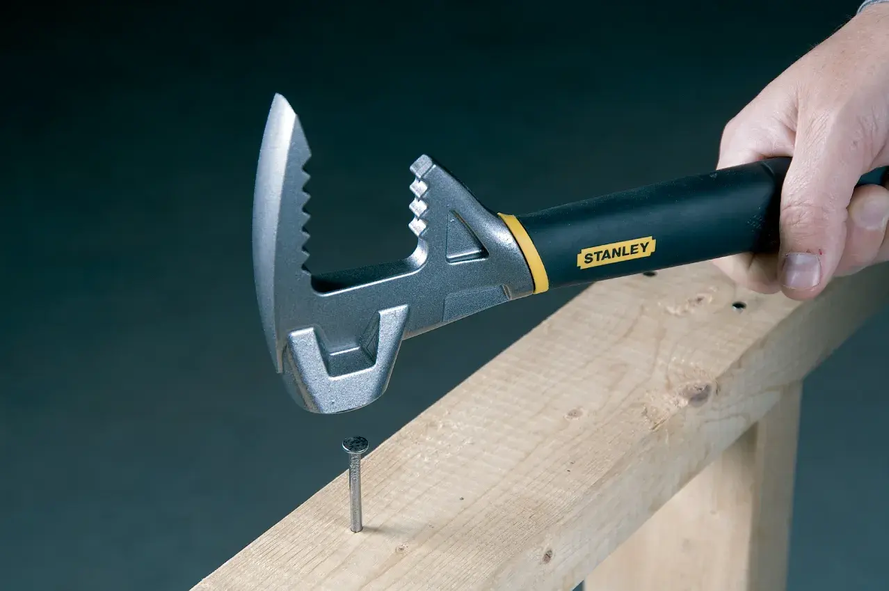 STANLEY 1-55-099 adjustable wrench with black handle, gripping a nail on wooden beam, close-up.