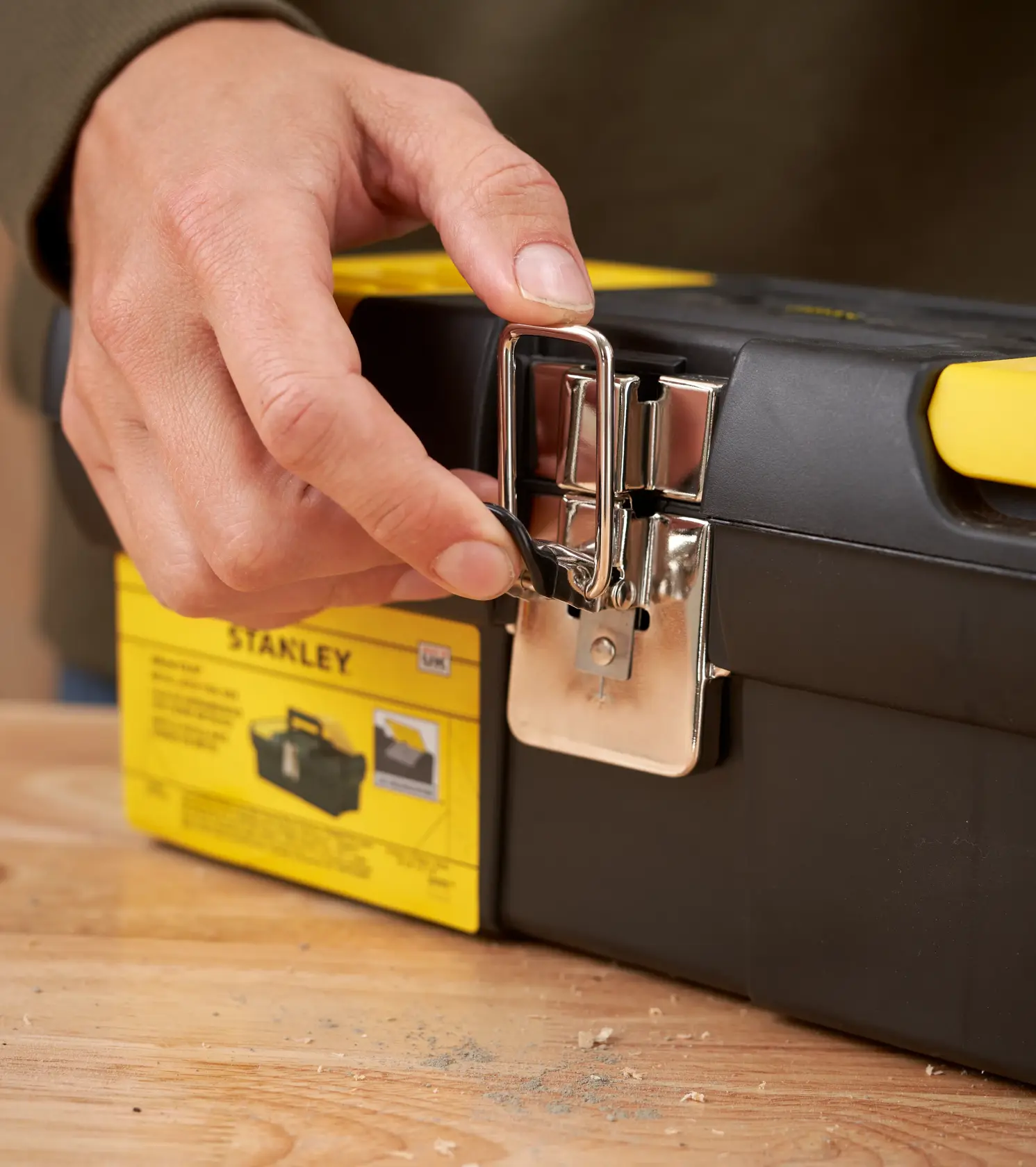 Photo of STANLEY 1-92-064 toolbox latch being opened by hand, black and yellow plastic toolbox on wood surface.