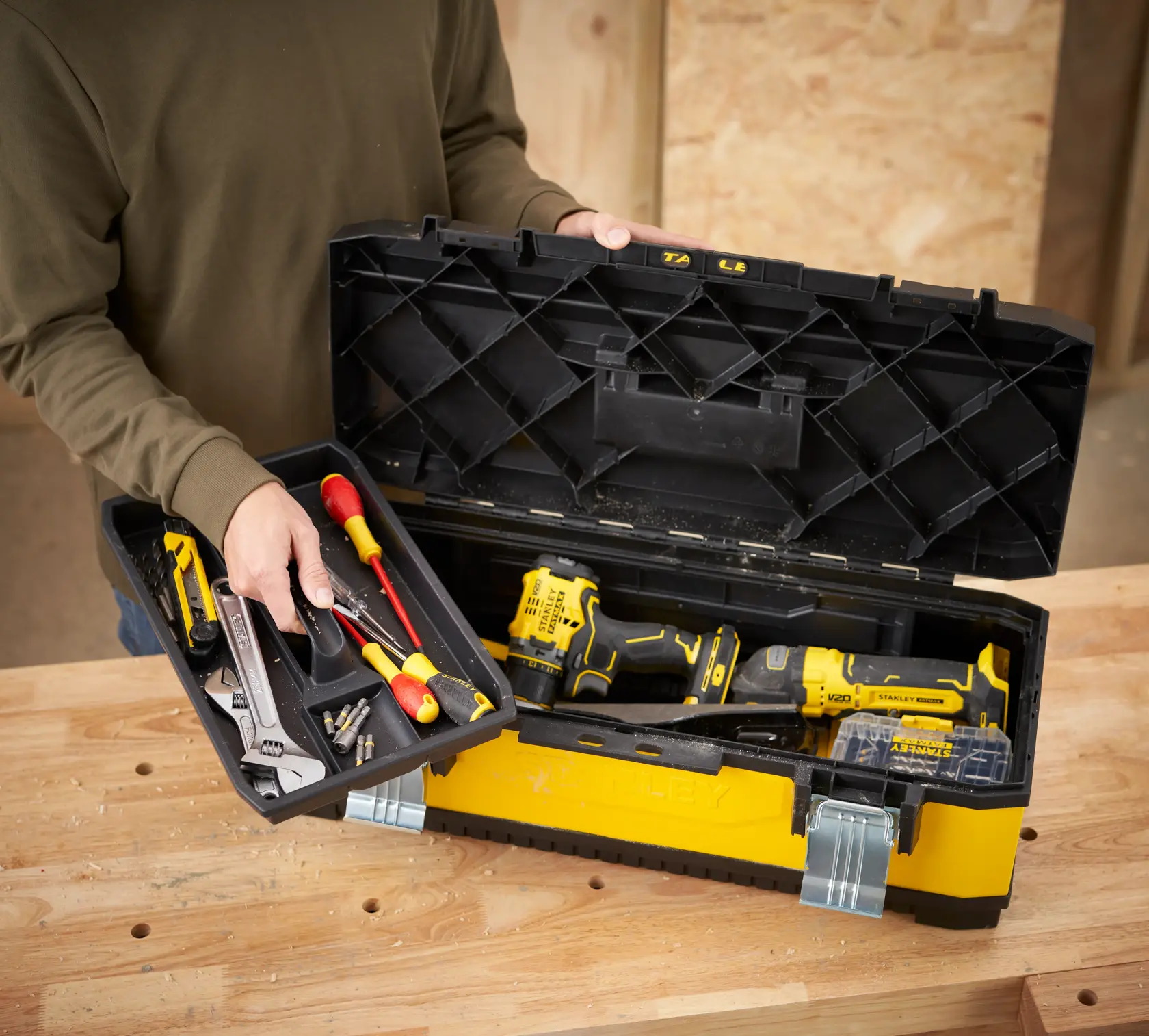 STANLEY 1-95-614 toolbox on workbench, lid open showing hand tools, screwdriver, wrench, and cordless drill inside.