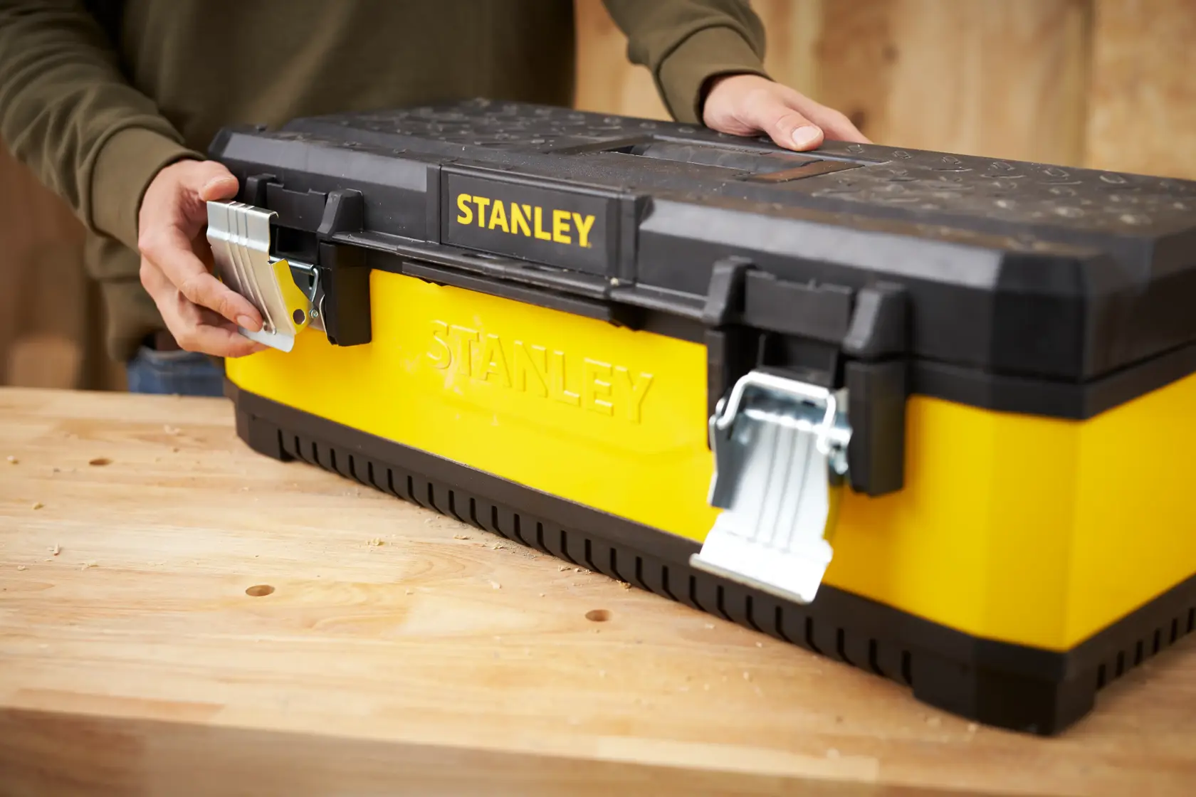 Photo of STANLEY 1-95-614 yellow and black toolbox with metal latches on a wooden workbench, front angle.