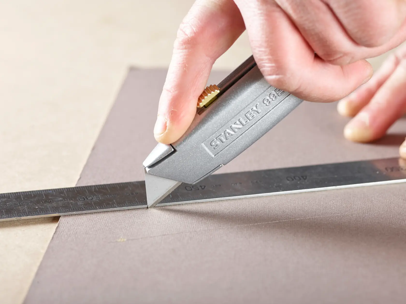 STANLEY 2-11-911 utility knife cutting material along metal ruler, close-up photography.