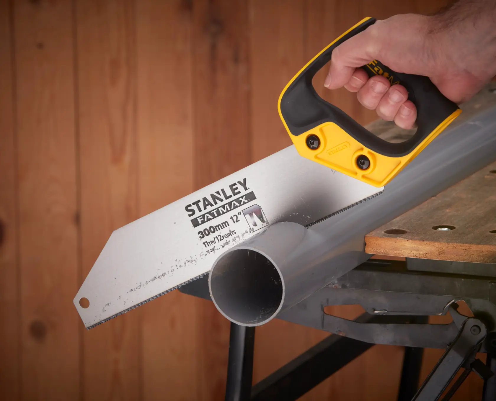 STANLEY 2-17-206 hand saw cutting plastic pipe on workbench, close-up view showing handle and blade.