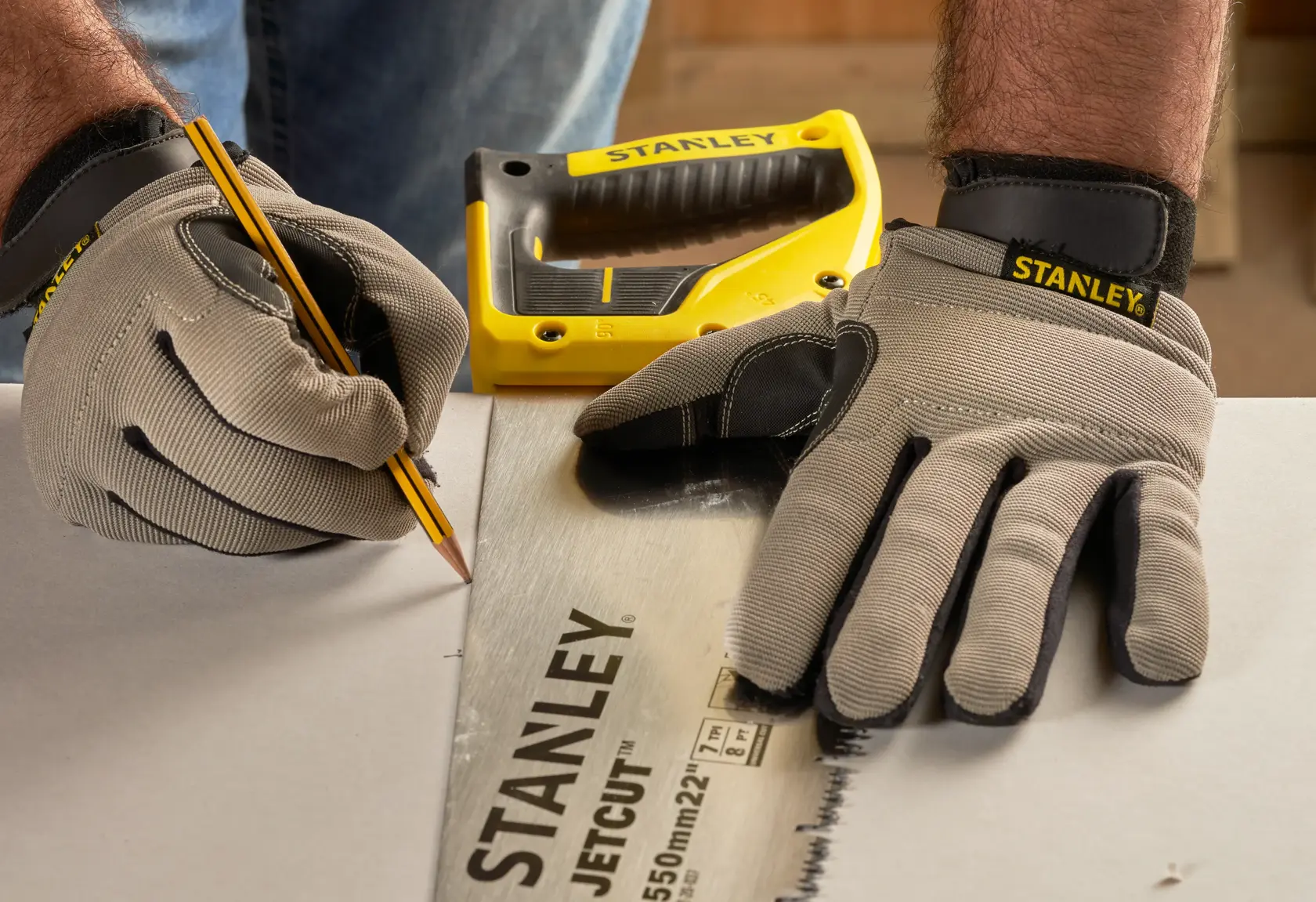 Stanley 2-20-037 JetCut handsaw on table, close-up angle, worker with gloves marking cut line.