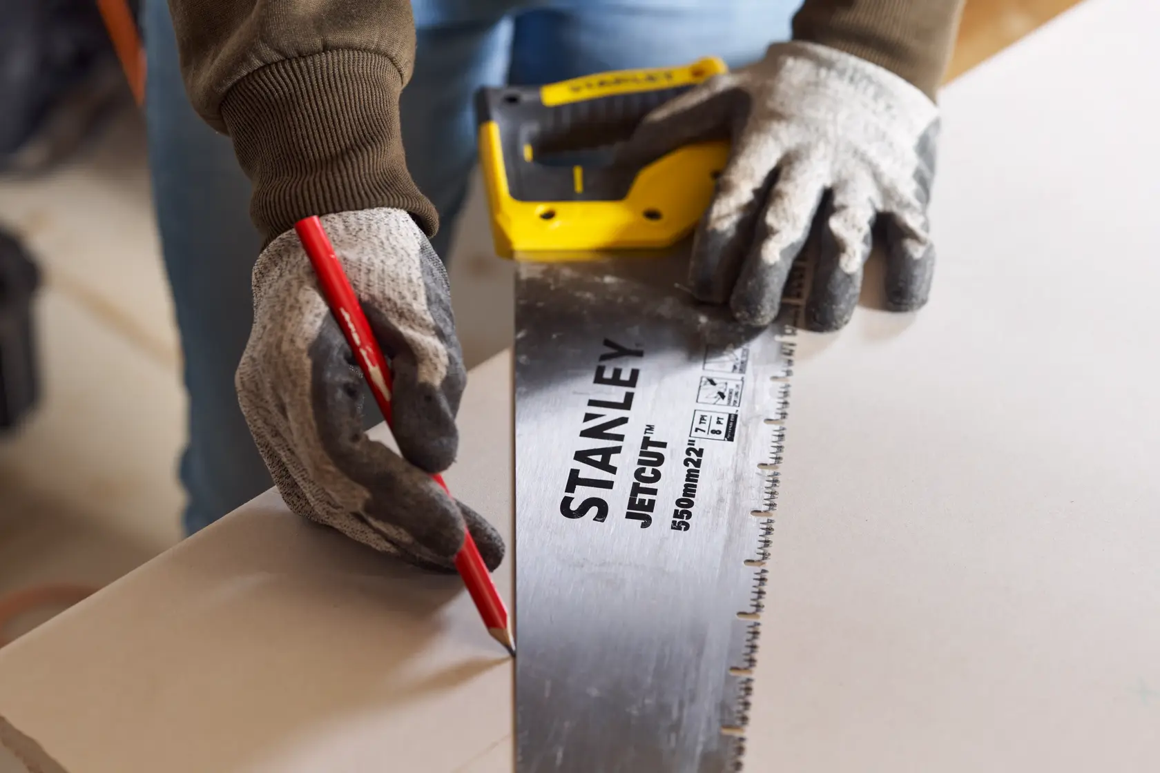 STANLEY 2-20-037 hand saw with yellow and black handle, user wearing gloves marking wood with a red pencil.