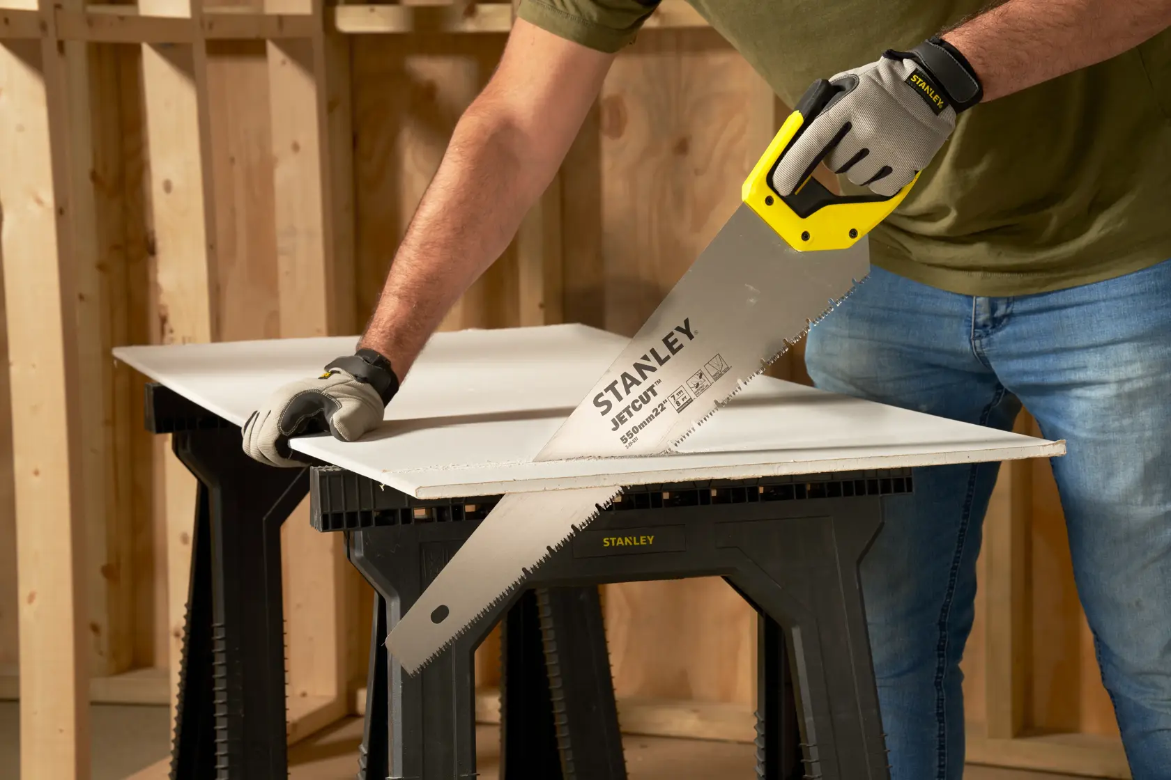 STANLEY 2-20-037 hand saw with yellow handle cutting drywall on black sawhorse, side angle.