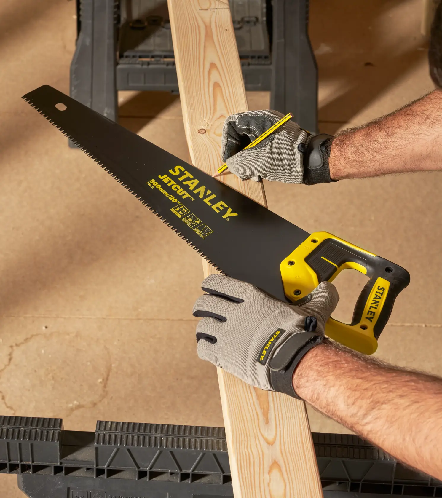 STANLEY 2-20-151 hand saw with yellow and black handle cutting a wooden plank, worker wearing gloves.