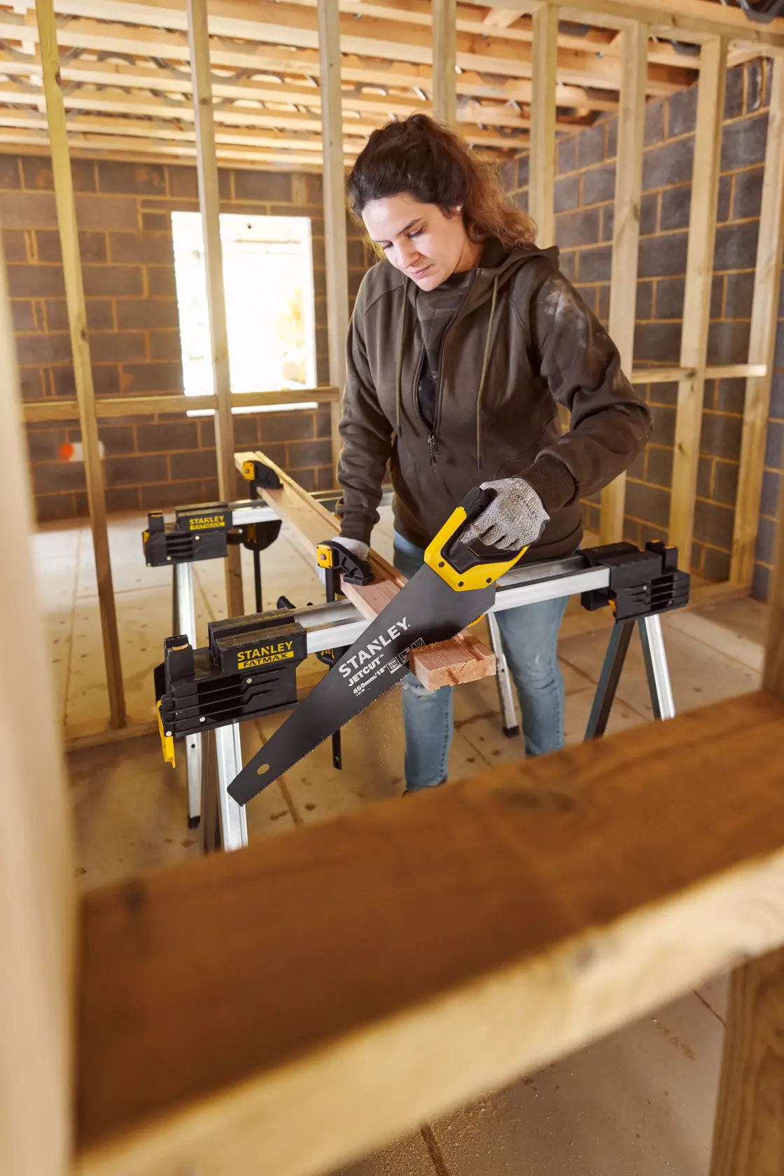 Photo of STANLEY 2-20-180 hand saw cutting wood on sawhorses inside a construction site.