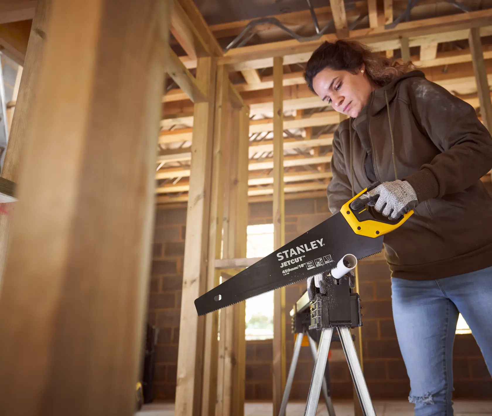 Photo of STANLEY 2-20-180 hand saw with yellow and black handle in use cutting plastic pipe on worksite.