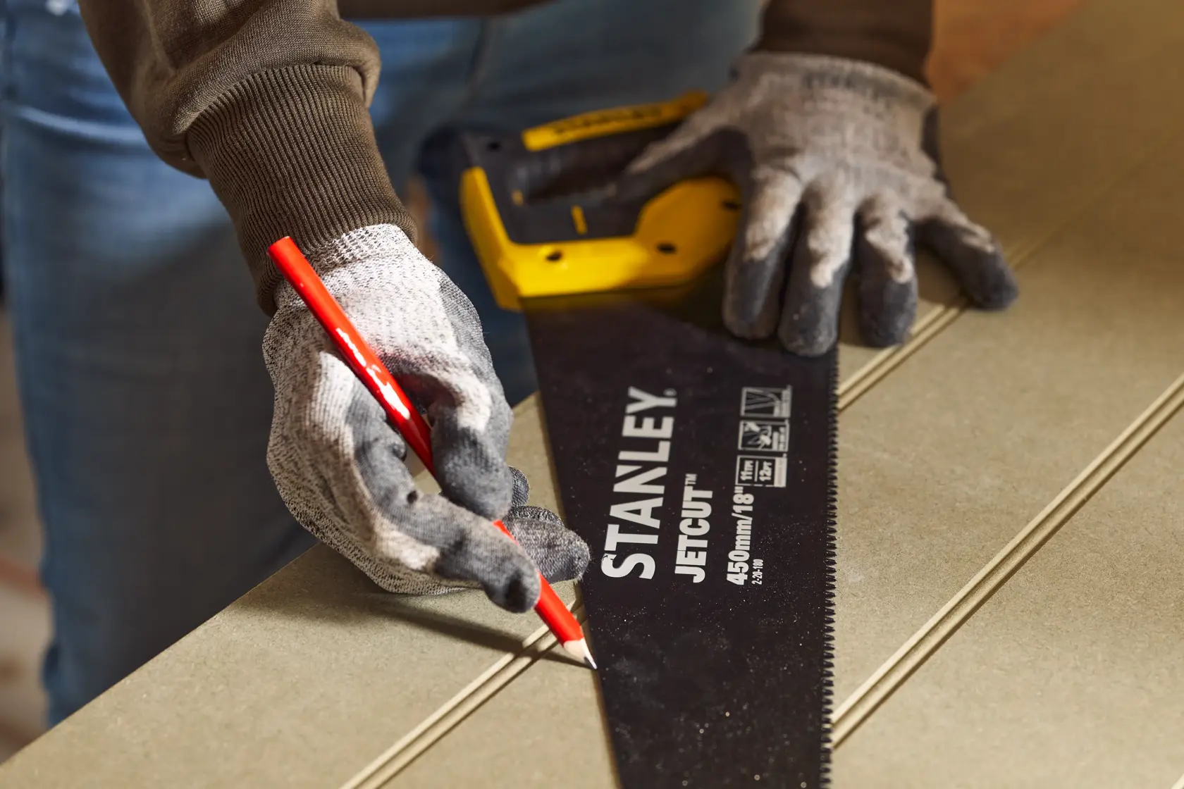 Photo of STANLEY 2-20-180 hand saw held by gloved hands, marking a line on wood with a red pencil.