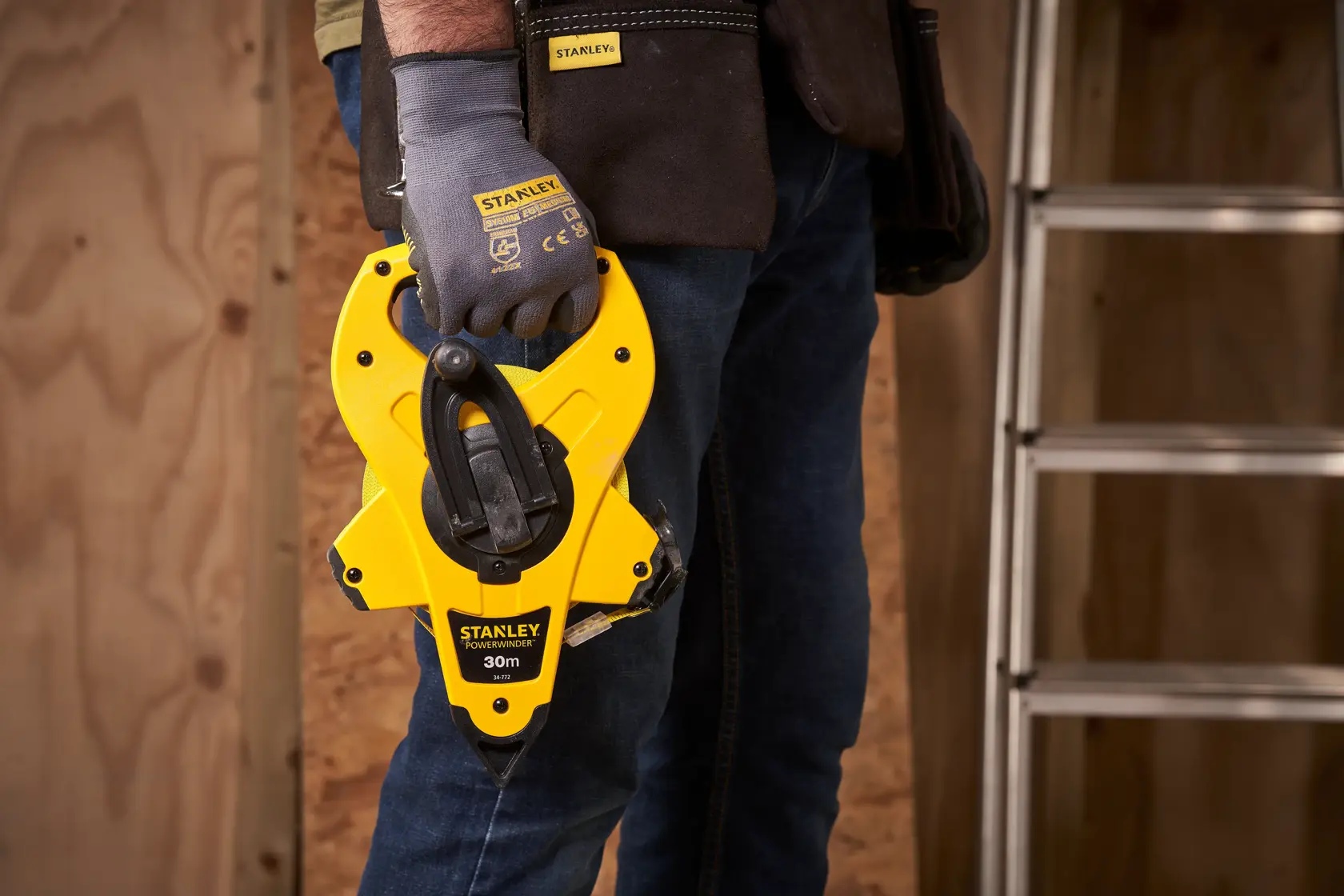 Photo of STANLEY 2-34-772 yellow 30m tape measure held by gloved hand at worksite.