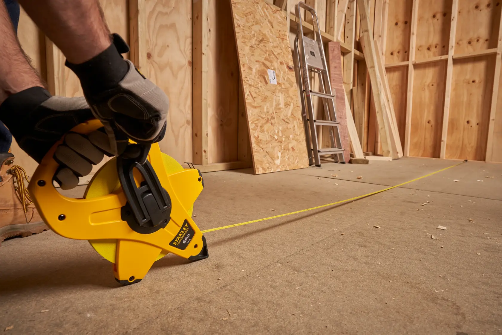 STANLEY 2-34-775 tape measure reel used on construction site, yellow casing, side angle view.