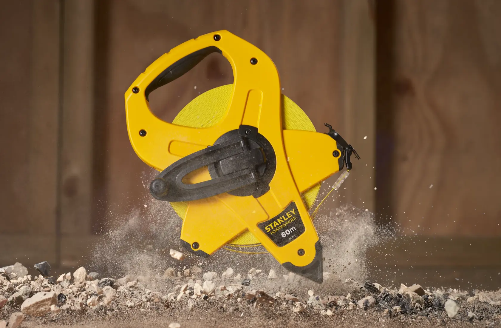STANLEY 2-34-775 open reel yellow measuring tape, 60m length, handheld with black handle, on construction debris.