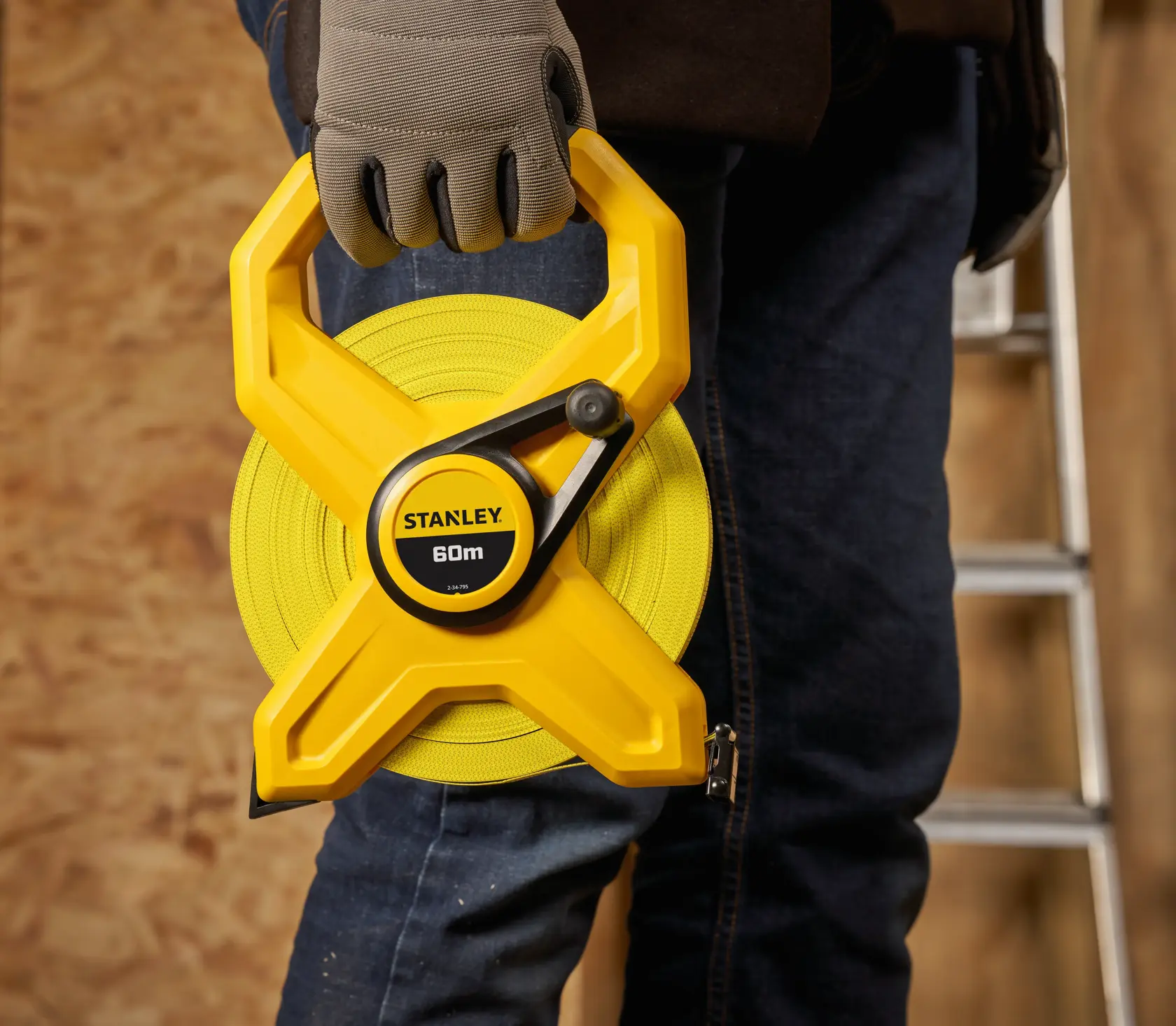 STANLEY 2-34-795 measuring tape 60m held by person wearing gloves, close-up, indoor work setting.
