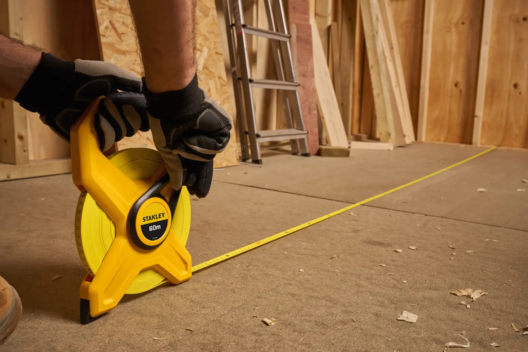 STANLEY 2-34-795 measuring tape reel used on construction site floor, yellow casing, close-up angle.