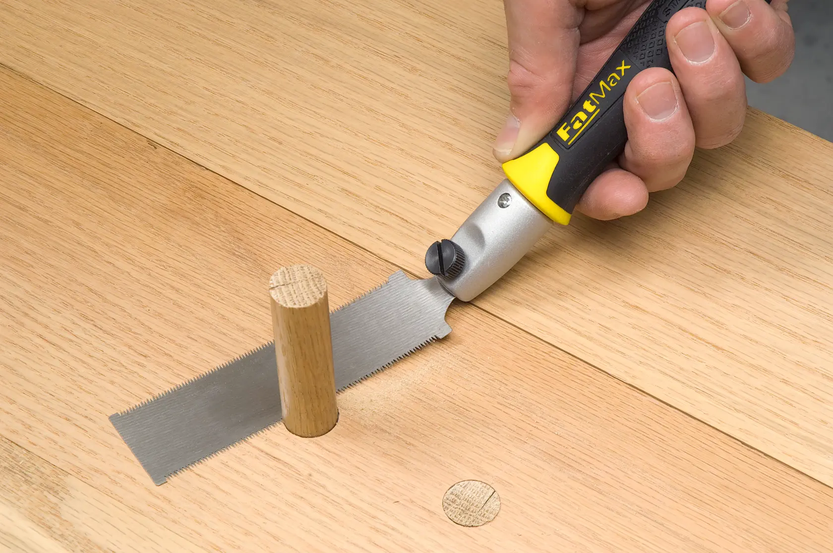 STANLEY 3-20-331 flush cut saw with yellow-black handle cutting wooden dowel on wooden surface.
