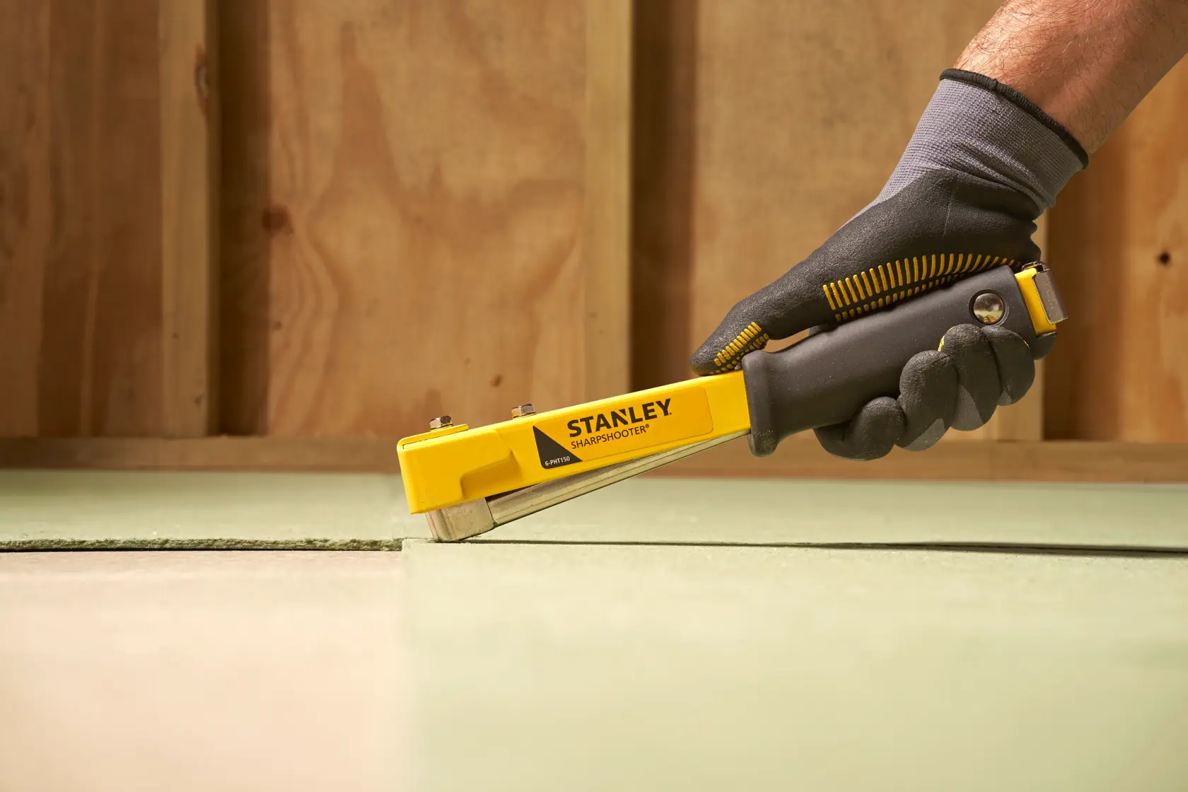 Photo of STANLEY 6-PHT150 staple gun being used on flooring, black and yellow design, side angle.