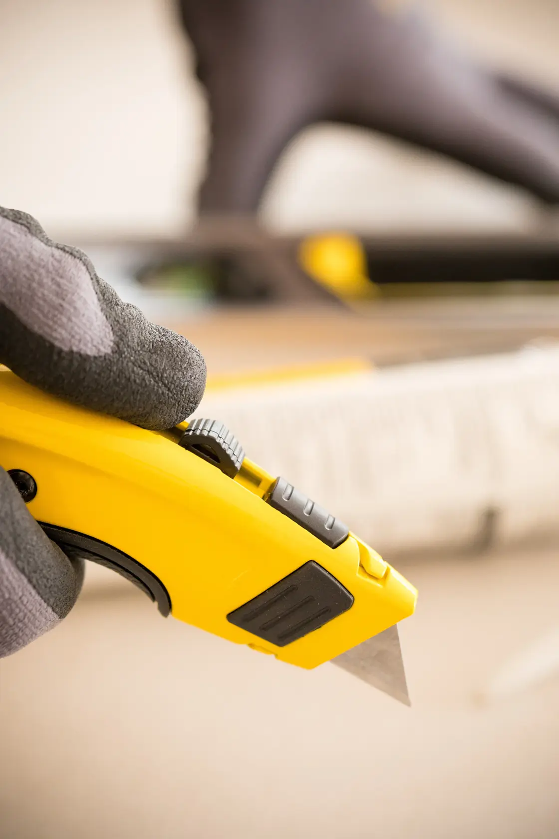 Close-up of STANLEY 7-10-778 utility knife held in gloved hand, yellow and black design, angled view.